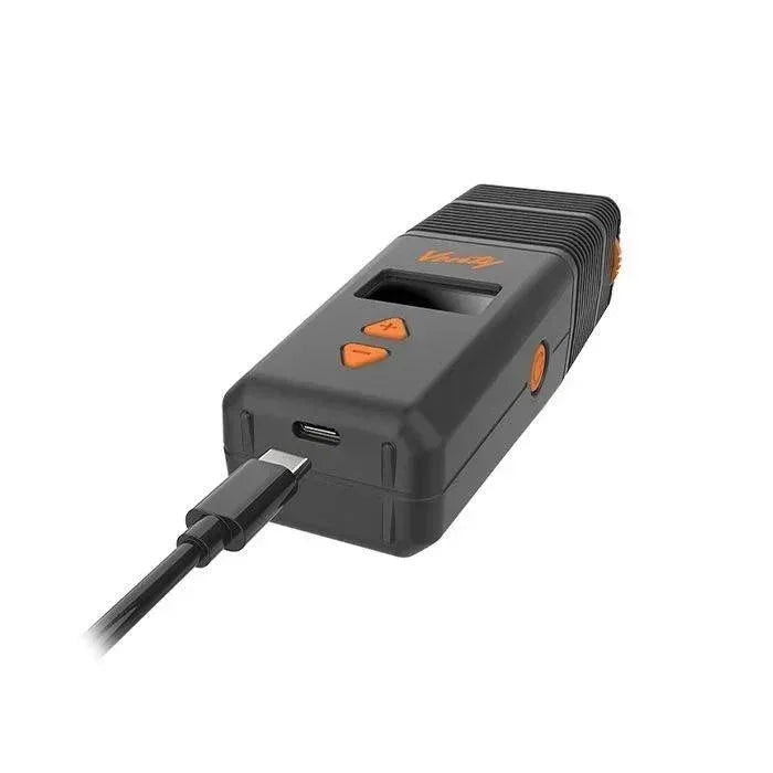 Portable vaporizer device charging via USB-C cable, black and orange accents, isolated view