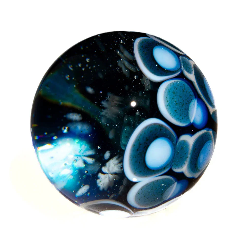 Hand-blown glass marble with blue, white, and teal abstract patterns on a dark background