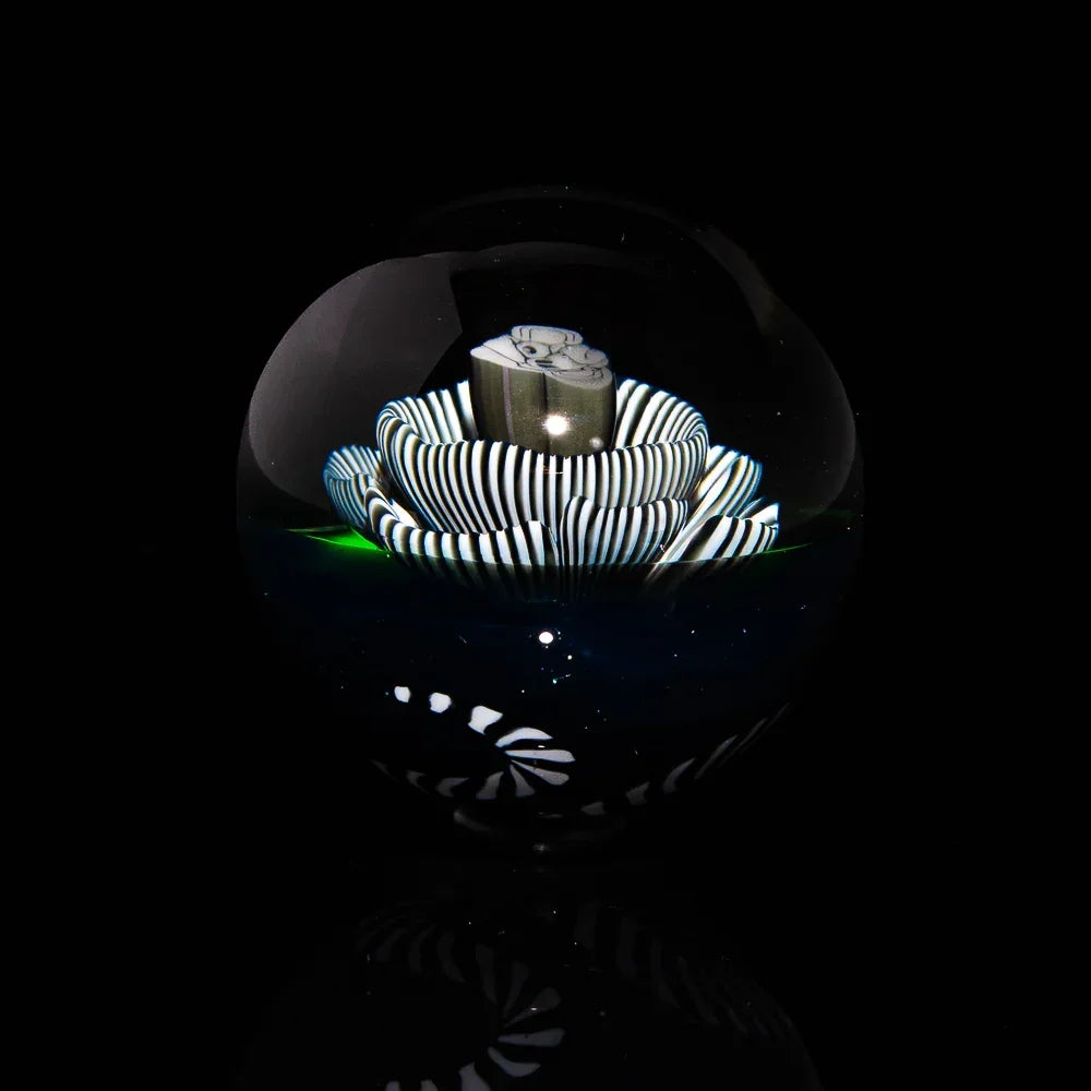 Handcrafted glass marble with black and white striped flower design on black background