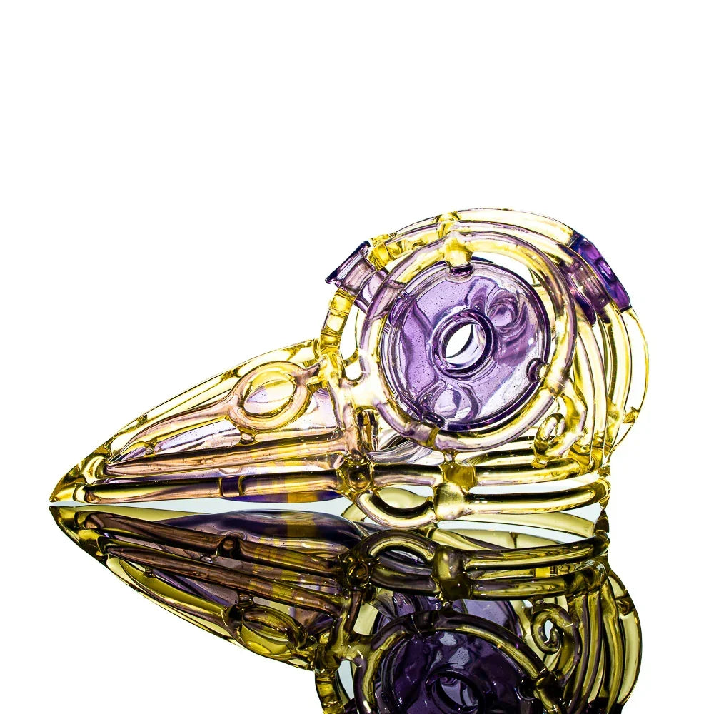 Colorful glass pipe shaped like a skull, yellow and purple, displayed on reflective surface.