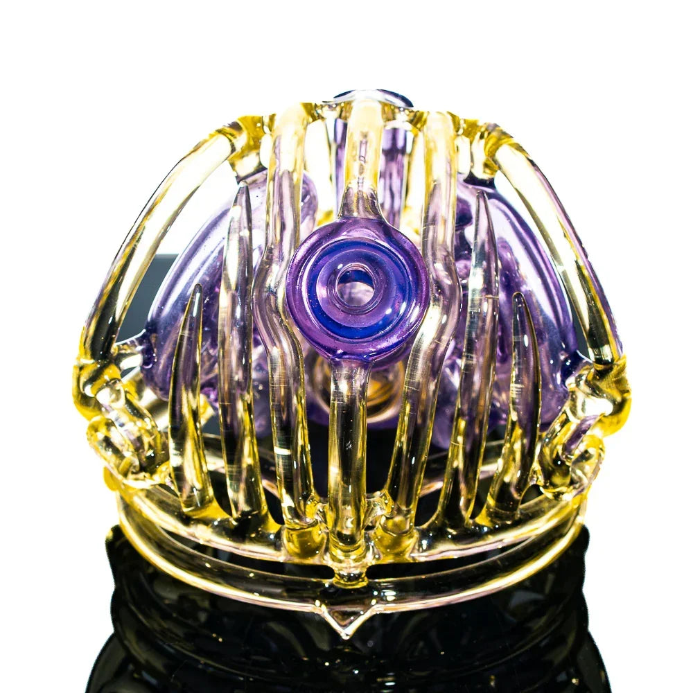 Intricate yellow and purple glass skull art piece with detailed ribbed design on reflective surface.