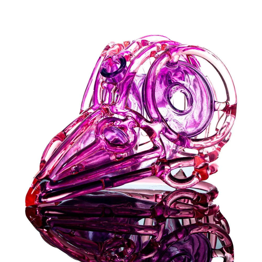 Purple glass art piece shaped like a bird skull on a reflective surface