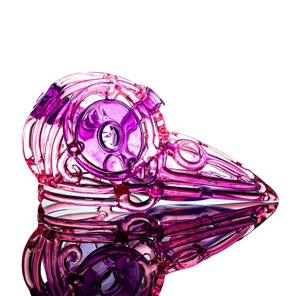 Pink glass skull pipe with intricate design, reflected on white background.