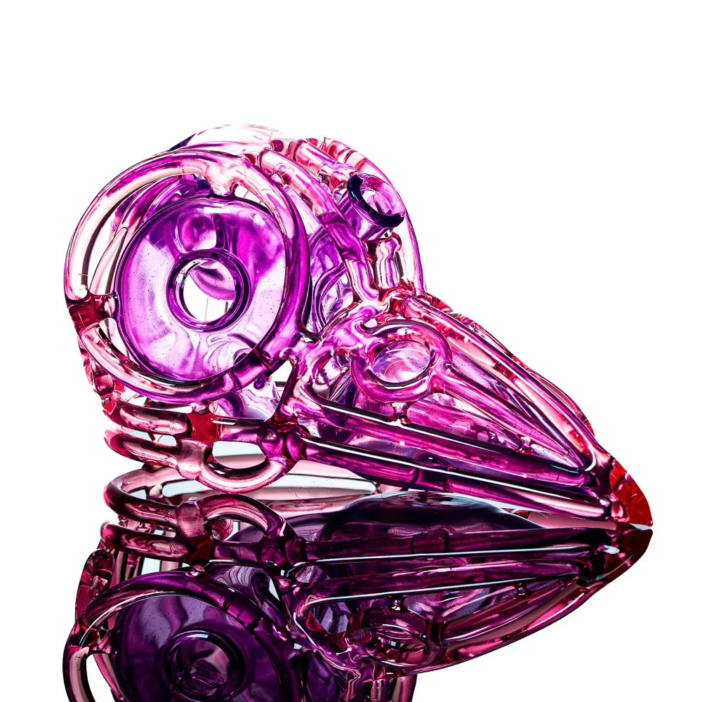 Purple glass skull pipe with bird beak design, displayed on a reflective surface