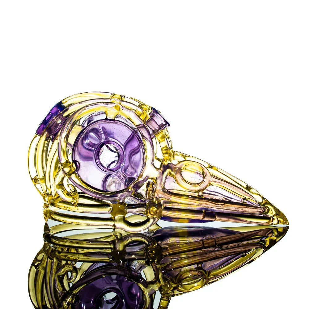 Yellow and purple glass art skull pipe with bird beak design, reflected on white background