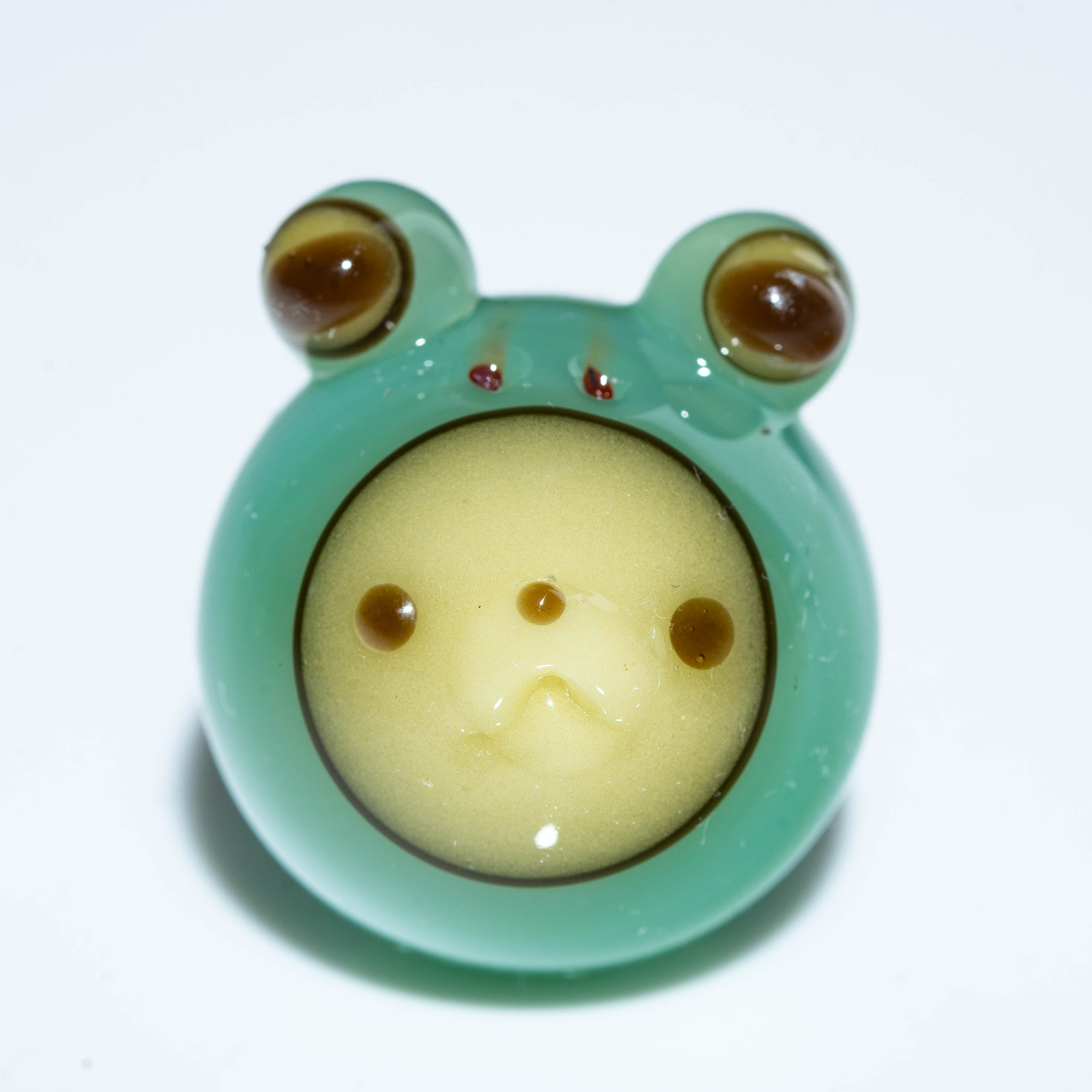 Handcrafted glass frog figurine with a round face and green body on white background