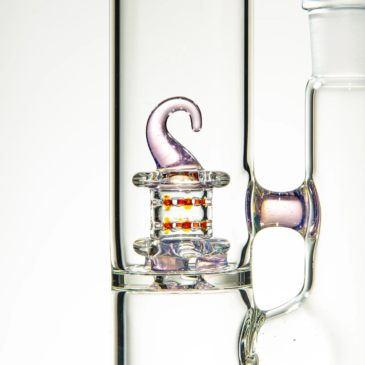 Close-up of a glass water pipe with a decorative pink hook and red bead accents inside.