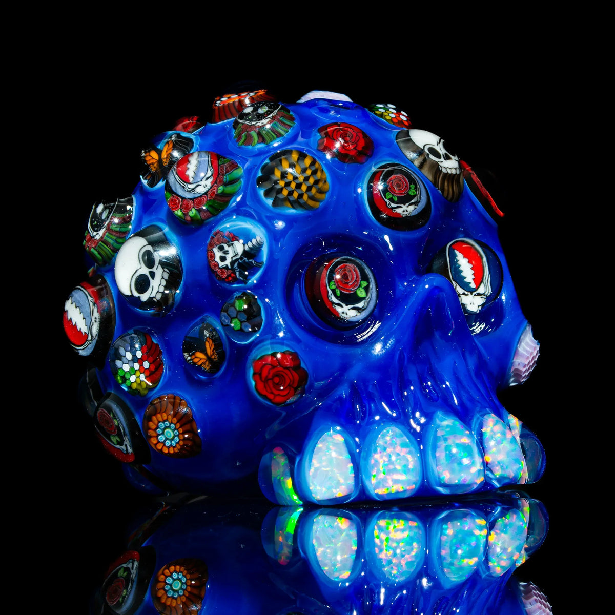 Blue glass skull art piece with colorful millefiori designs and opal teeth on black background