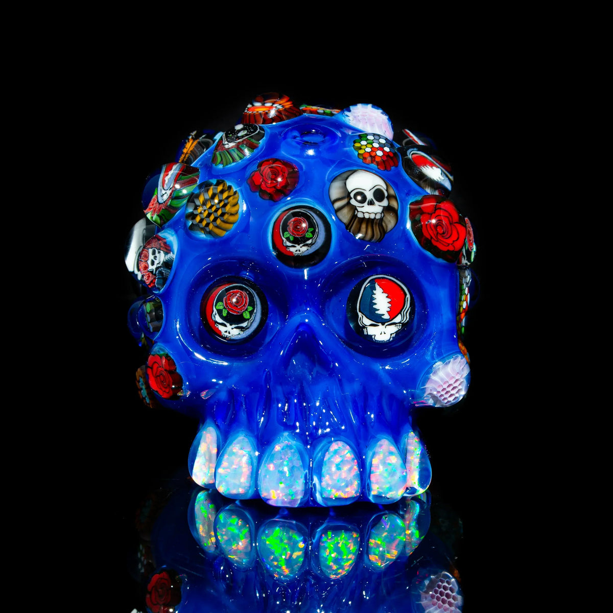 Blue glass skull art piece with colorful embedded cabochons, roses, and psychedelic designs