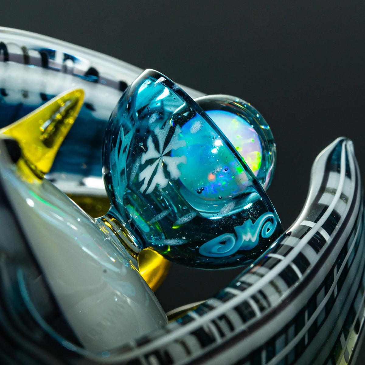 Close-up of intricate glass art pipe with blue, yellow, and white details, snowflake design