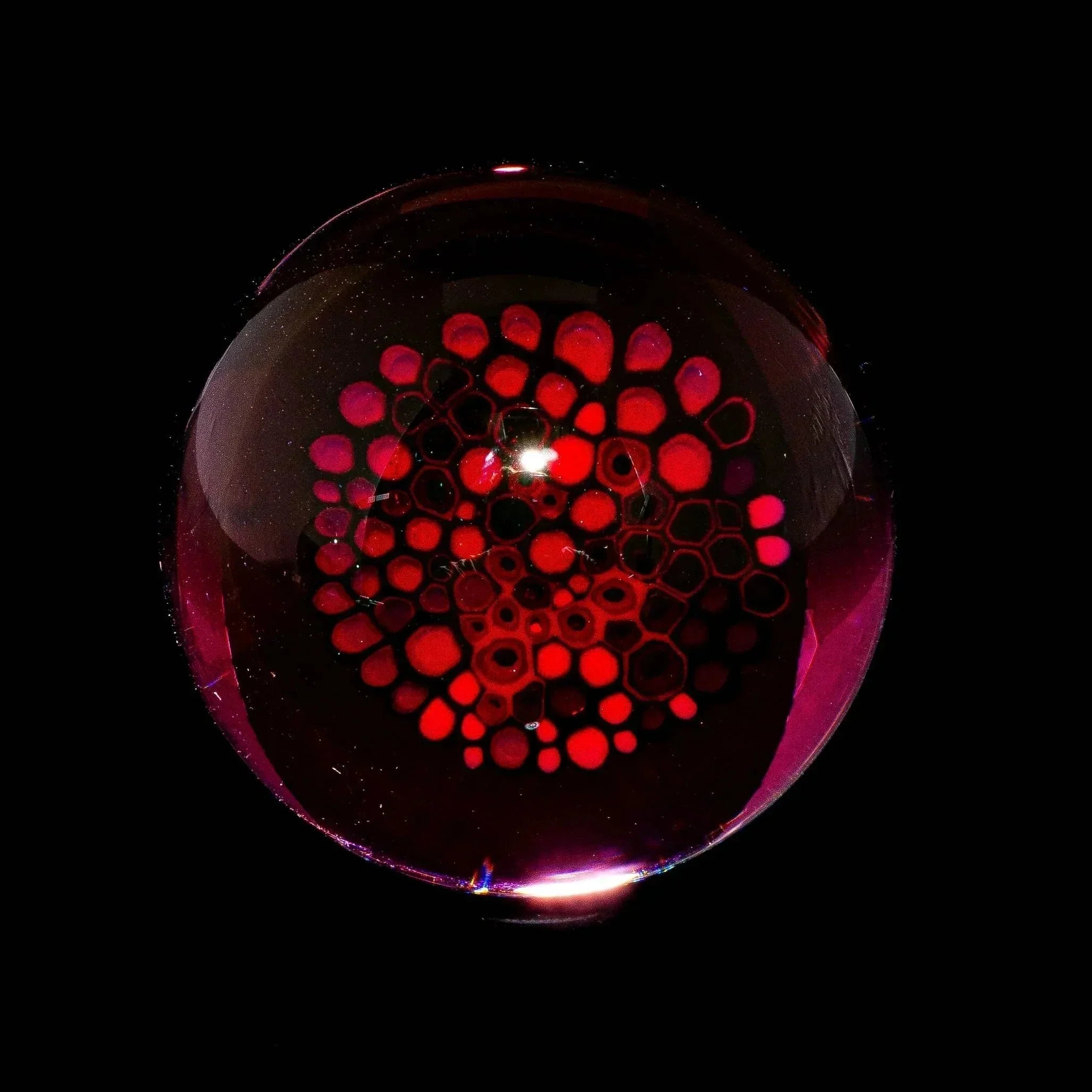 Handcrafted glass marble with intricate red honeycomb pattern on black background