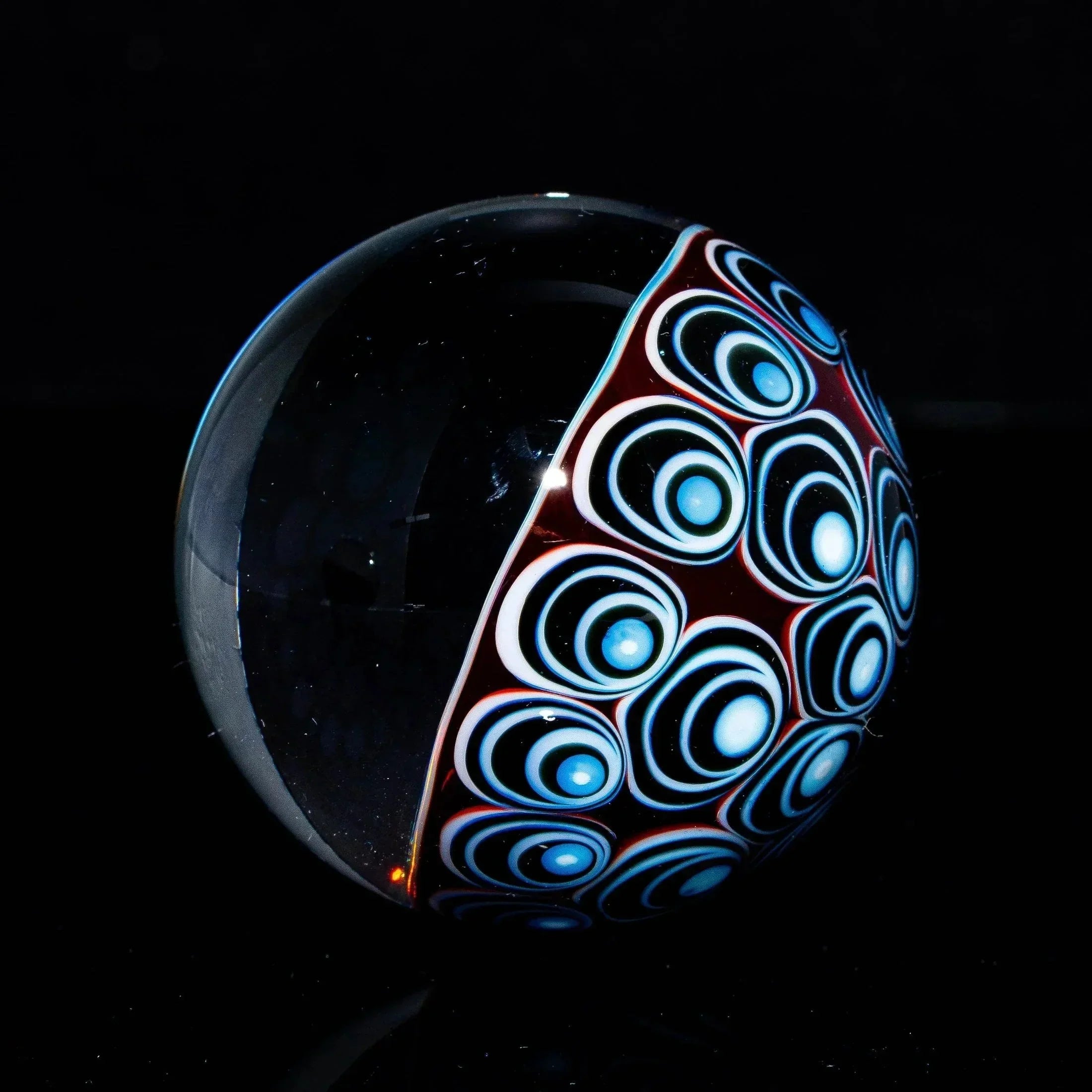 Handmade glass marble with colorful blue and white patterned design on a black background