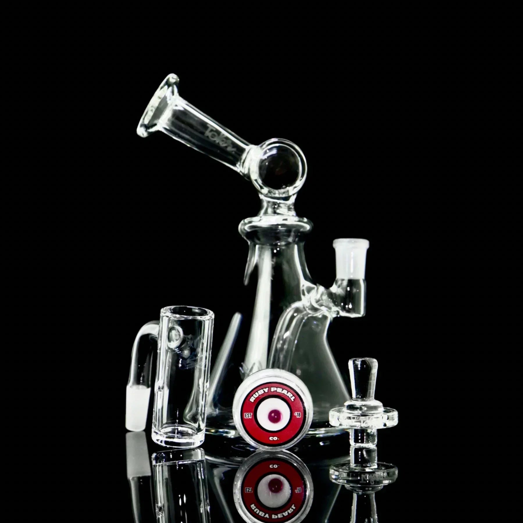 Clear glass dab rig with quartz banger, carb cap, and Ruby Pearl accessory on black background