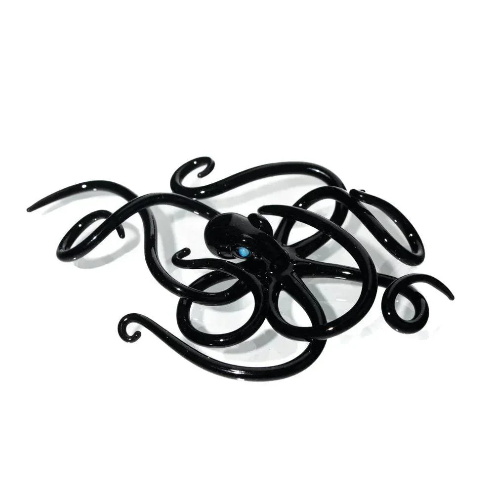 Black glass octopus figurine with blue eyes and curled tentacles on white background