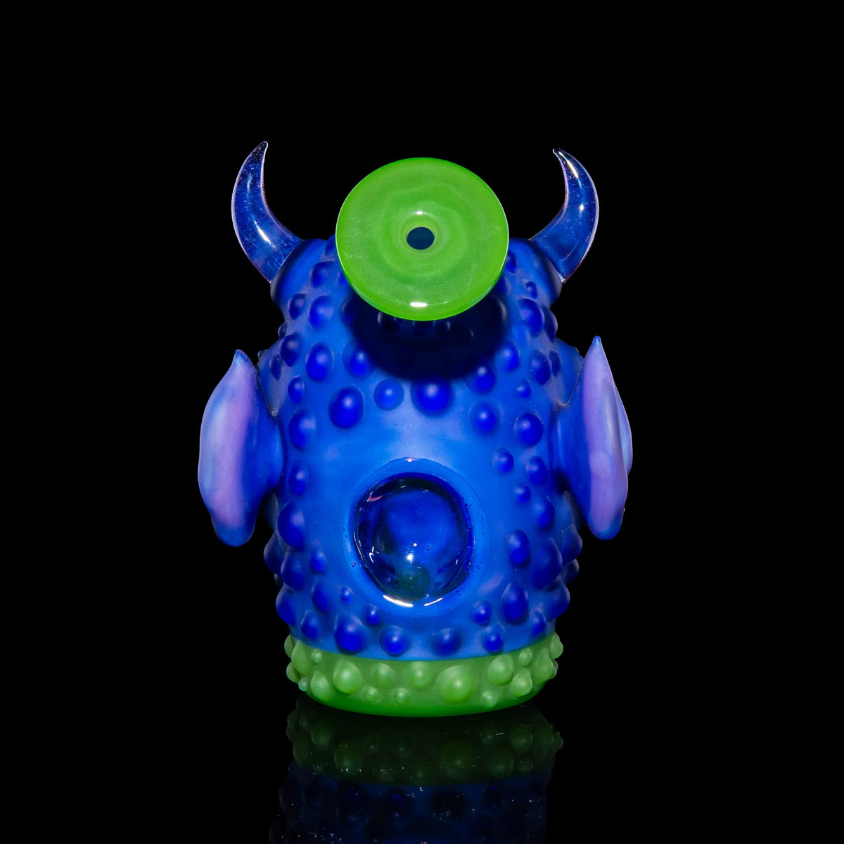 Colorful glass monster pipe with one eye, horns, and textured blue and green body on black background