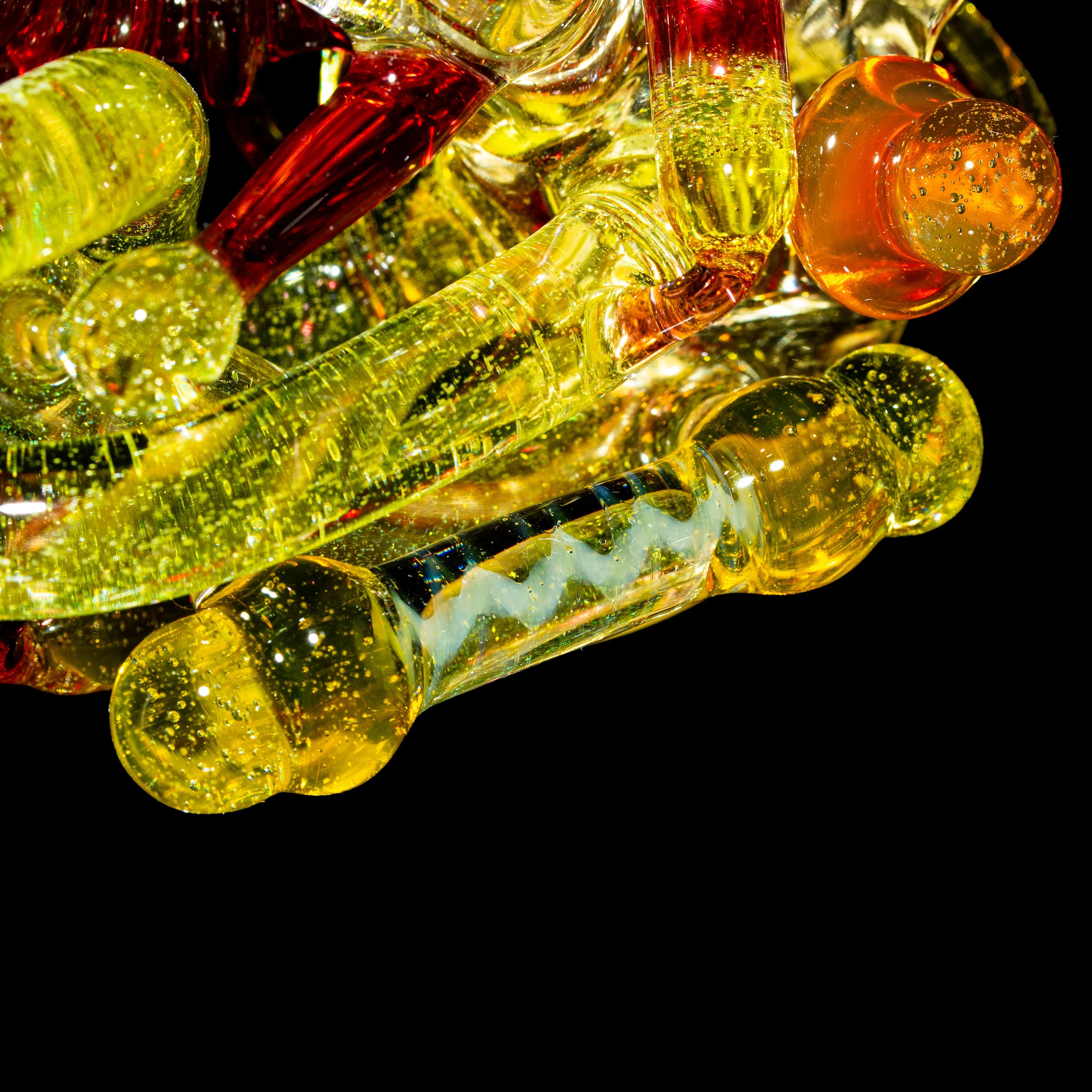 Close-up of yellow and orange hand-blown glass pipes with sparkling details on black background