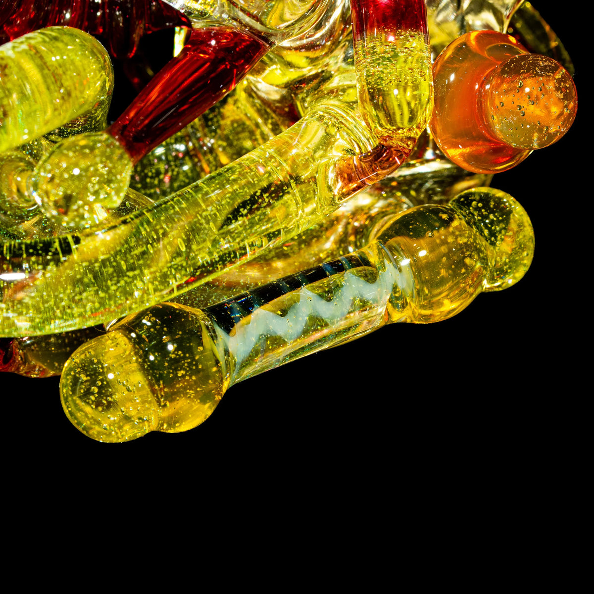 Close-up of yellow and orange hand-blown glass pipes with sparkling details on black background