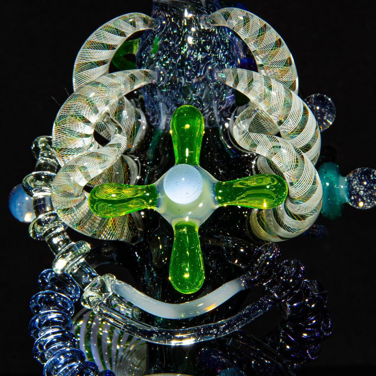 Intricate heady glass art piece with green, clear, and spiral accents against black background