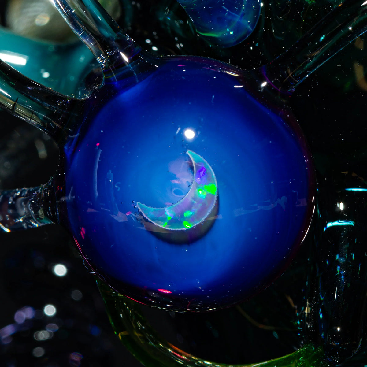 Close-up of a blue glass art piece with a crescent moon and iridescent accents