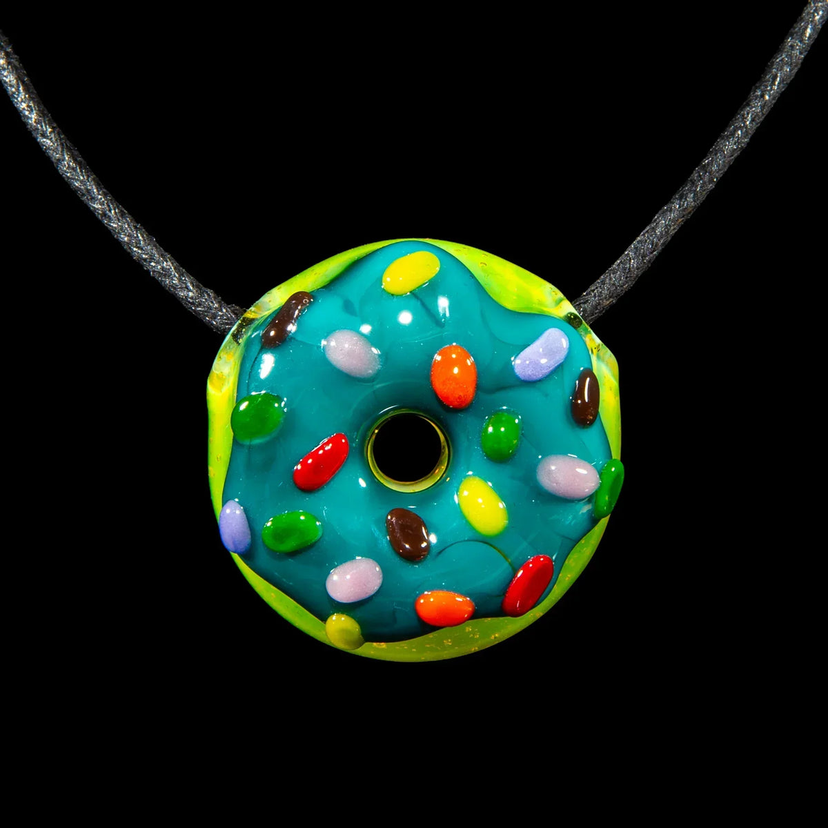 Colorful glass donut pendant necklace with teal glaze and candy sprinkles on black background