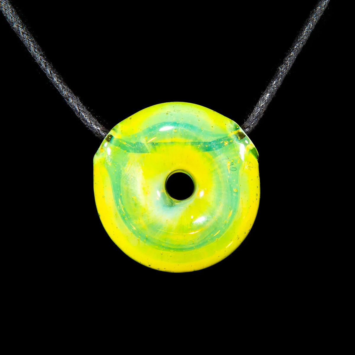 Yellow and green glass donut pendant necklace on black cord, isolated on black background