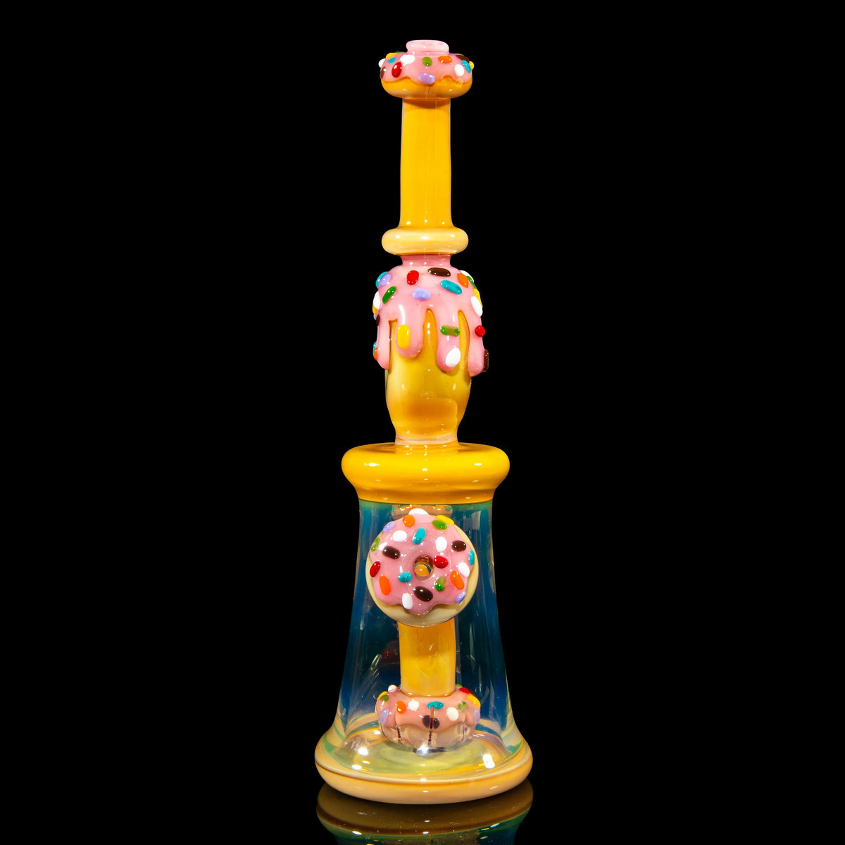 Colorful donut-themed glass water pipe with sprinkles and yellow, pink accents on black background.
