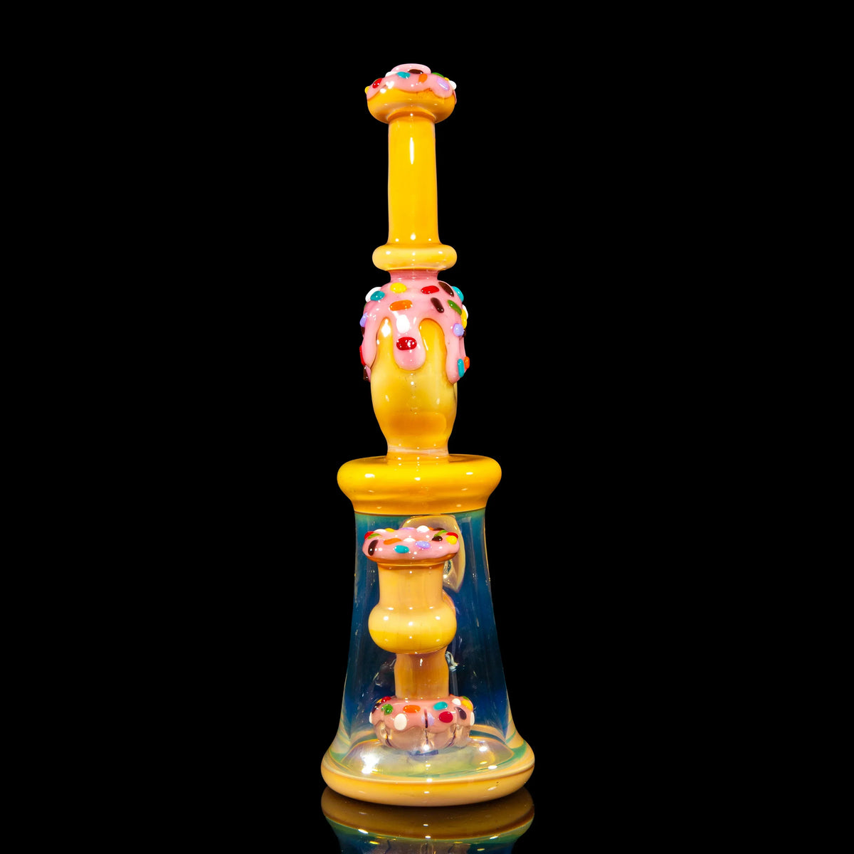 Colorful donut-themed glass bong with yellow base, pink icing, and sprinkles on black background
