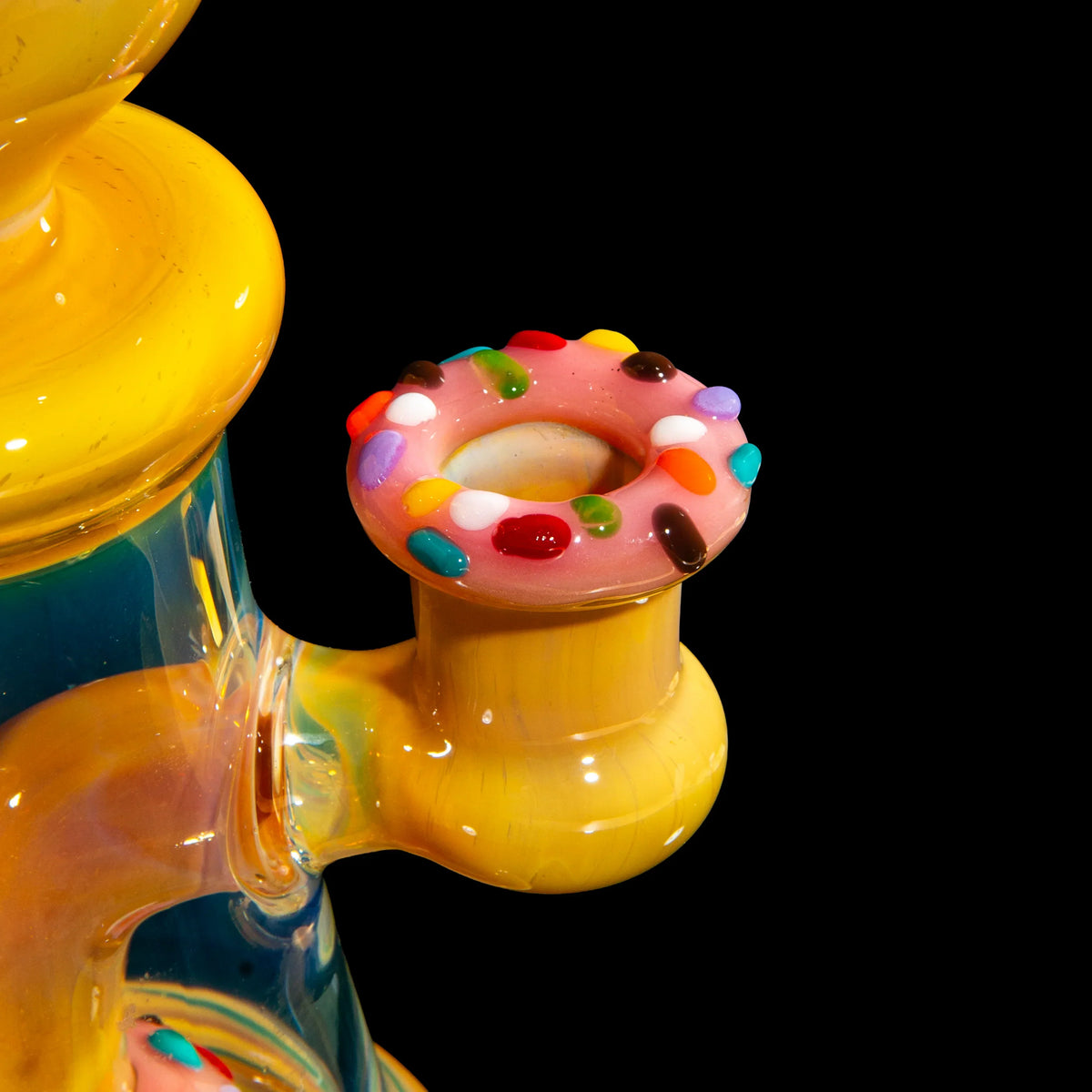Colorful glass water pipe with donut-themed bowl and candy accents on black background