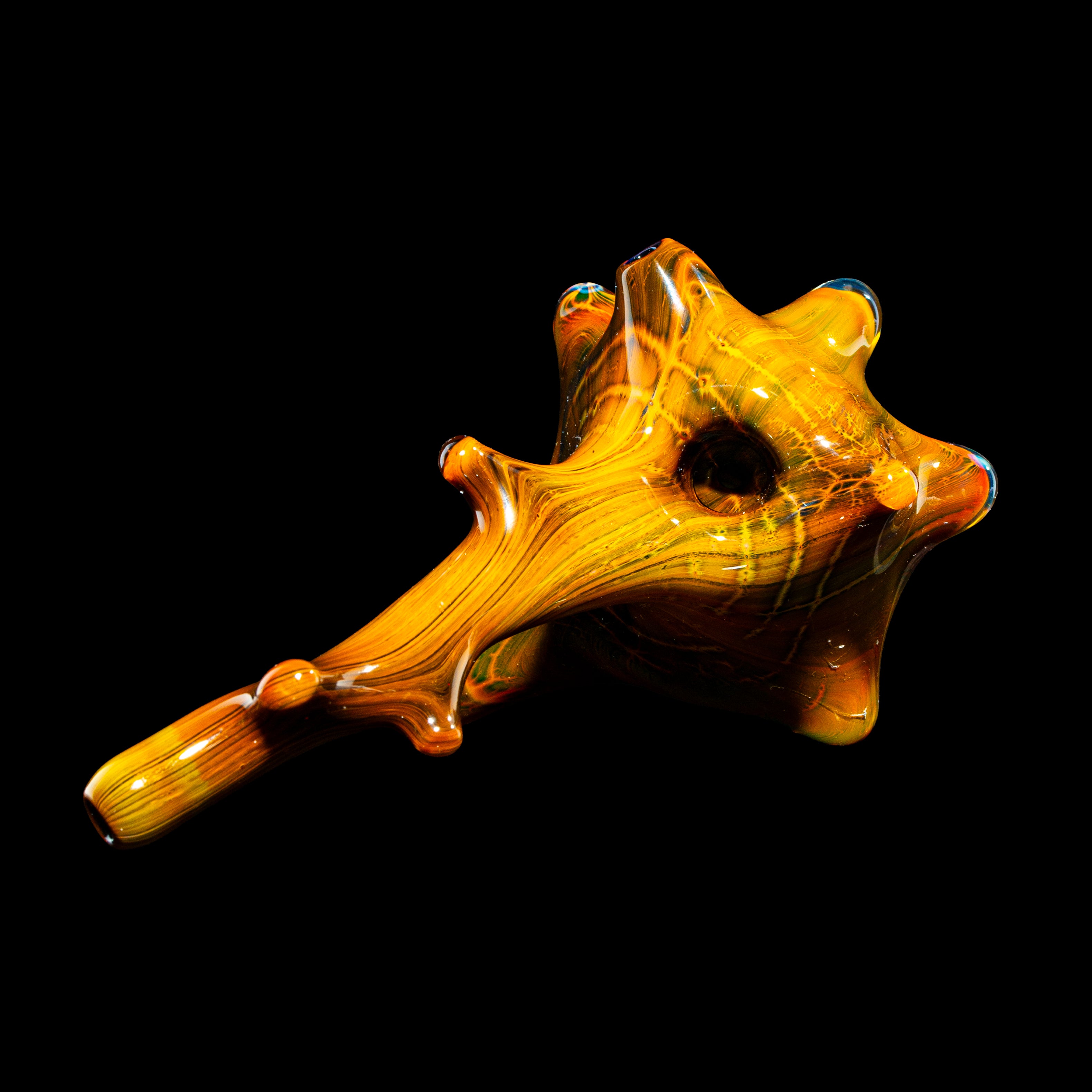 Hand-blown amber glass pipe with sculpted, spiked design on black background