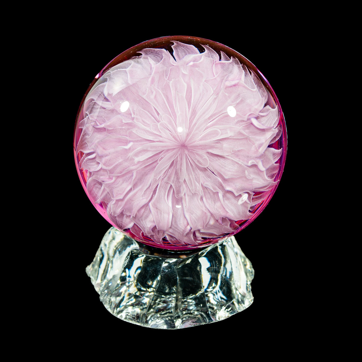 Pink and clear glass art sphere with intricate flower design, displayed on glass stand