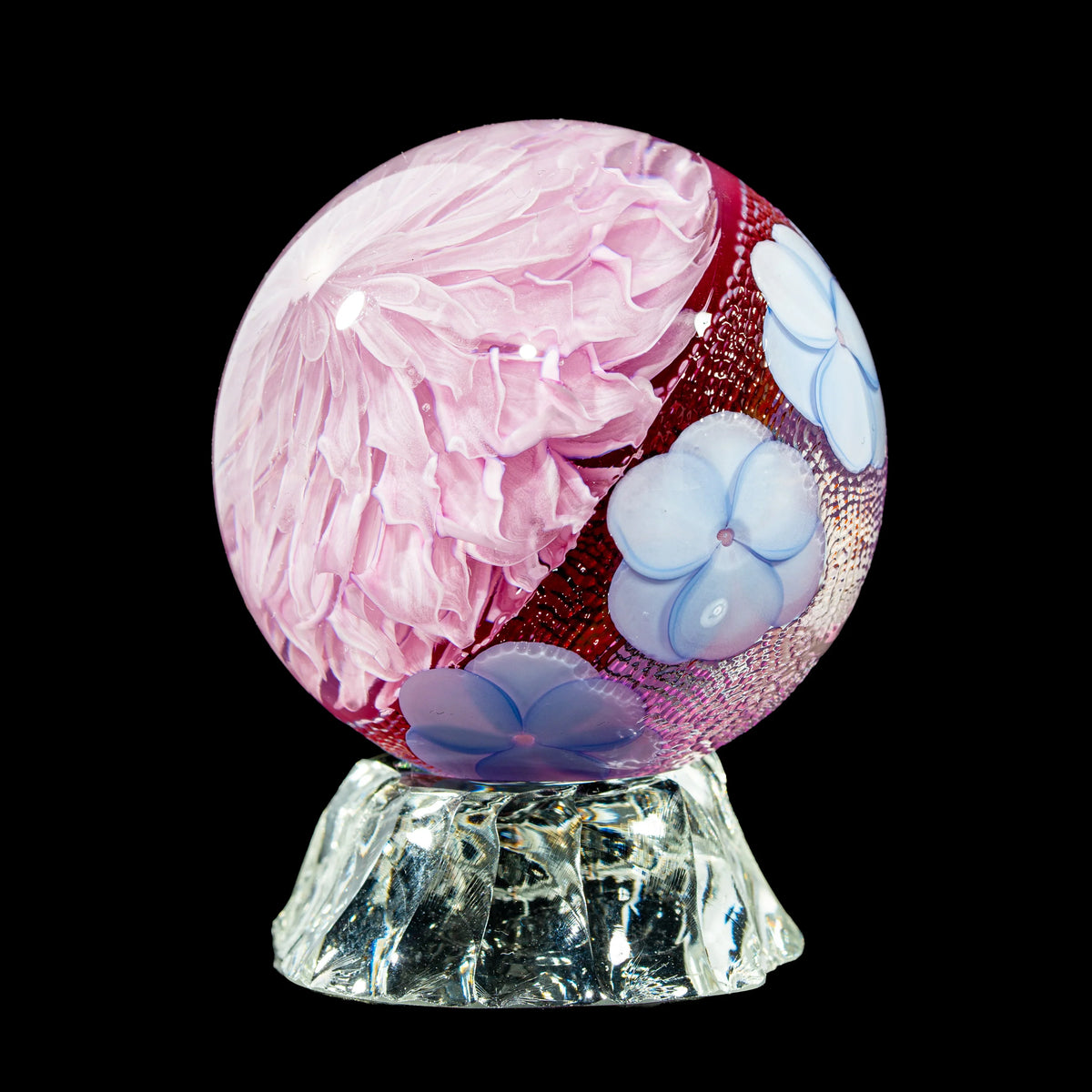 Handcrafted glass sphere with pink floral design and blue flower accents on clear stand