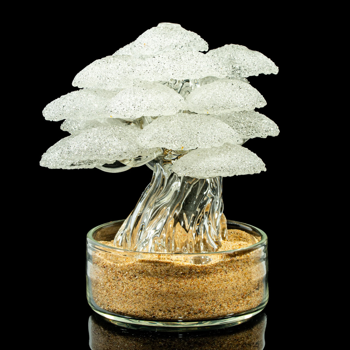 Intricate clear glass art tree sculpture with textured branches in sand, on black background
