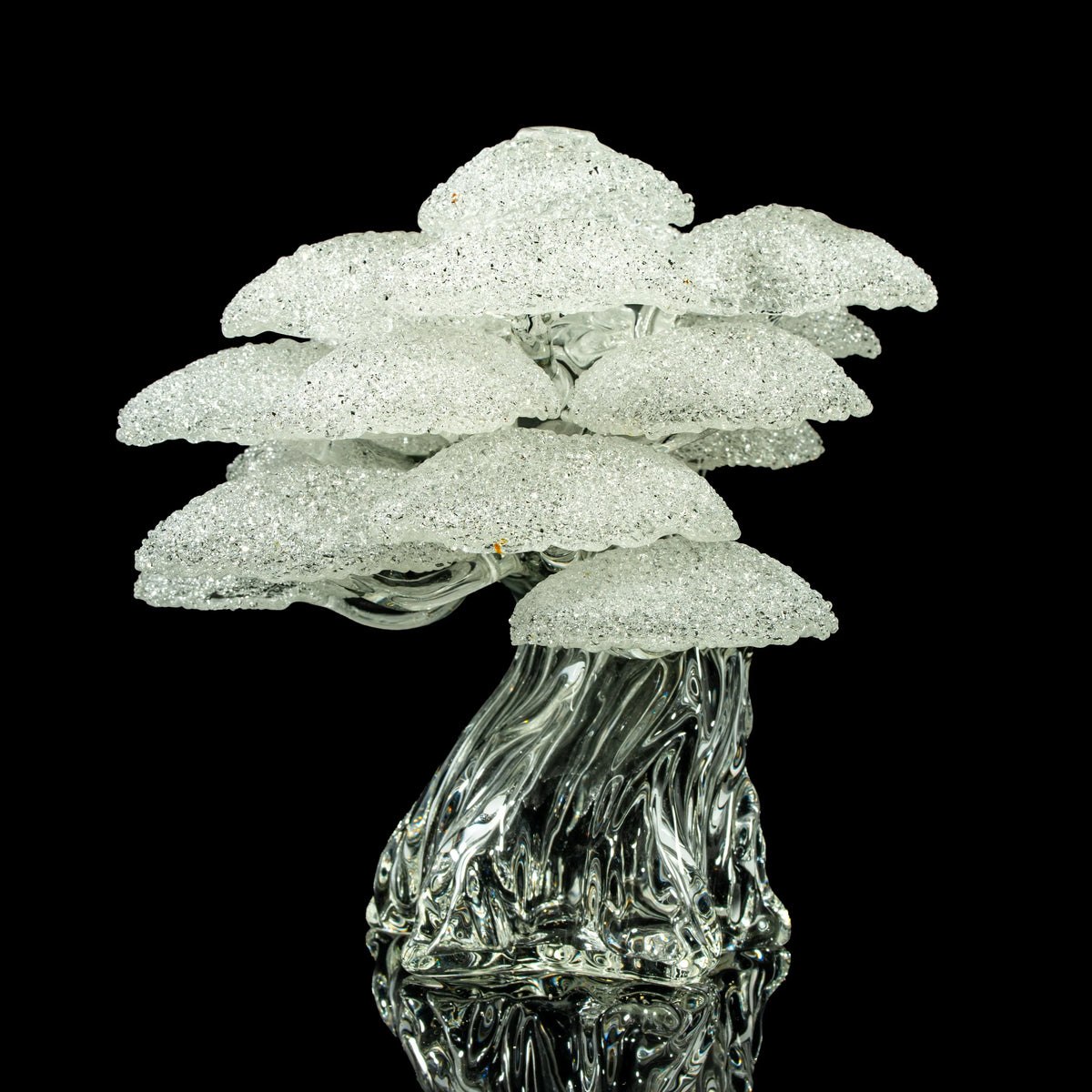 Clear textured glass art sculpture shaped like a cluster of mushrooms on a black background.