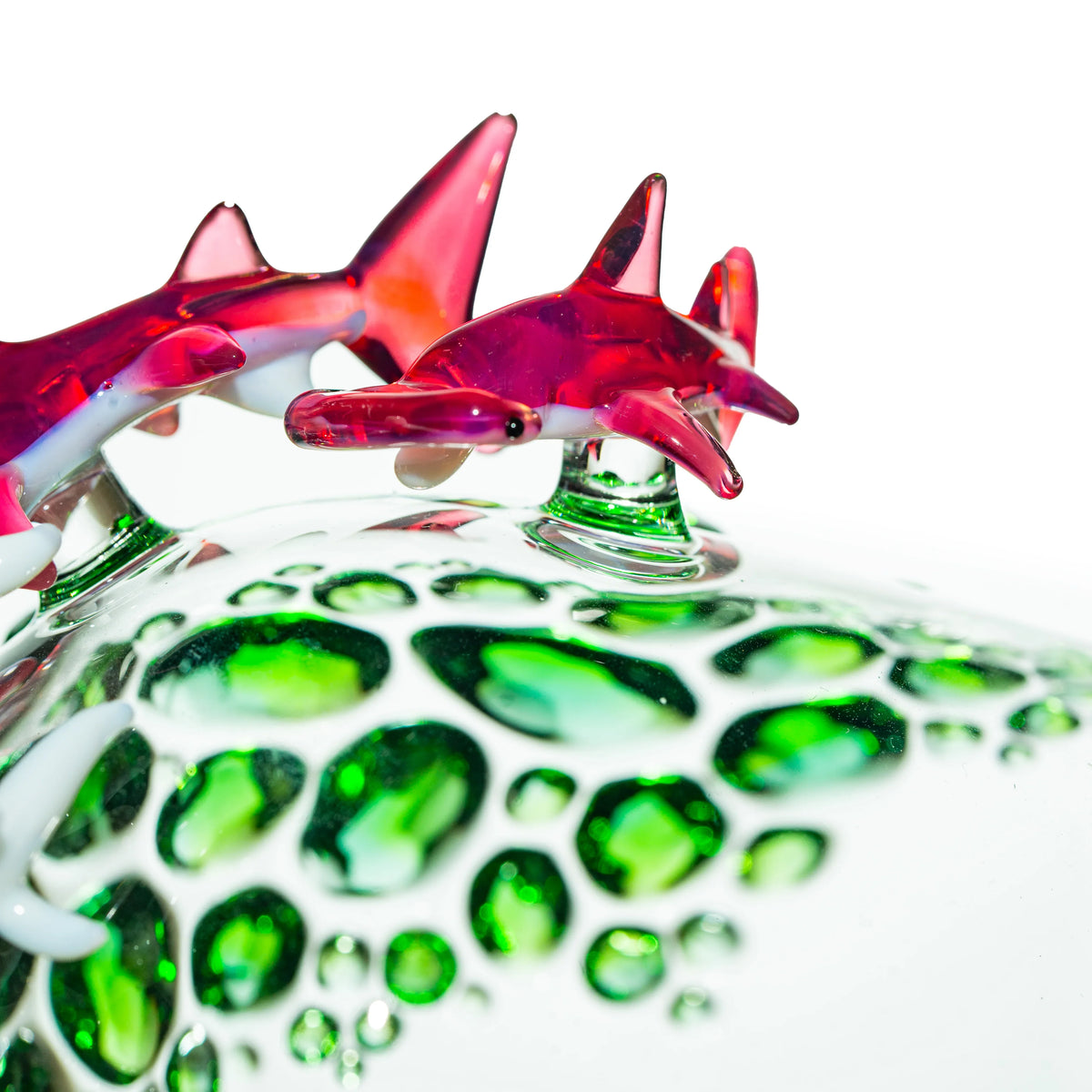Handcrafted glass art piece with red sharks and green bubble accents on clear glass.