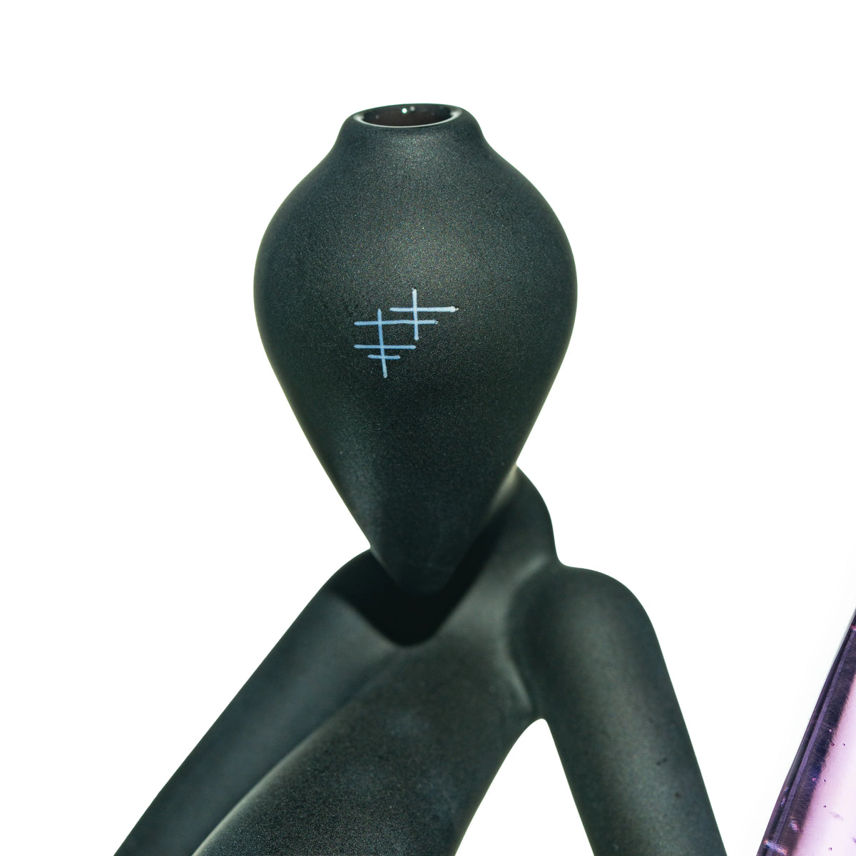 Close-up of a matte black glass sculpture with minimalist blue line design, white background