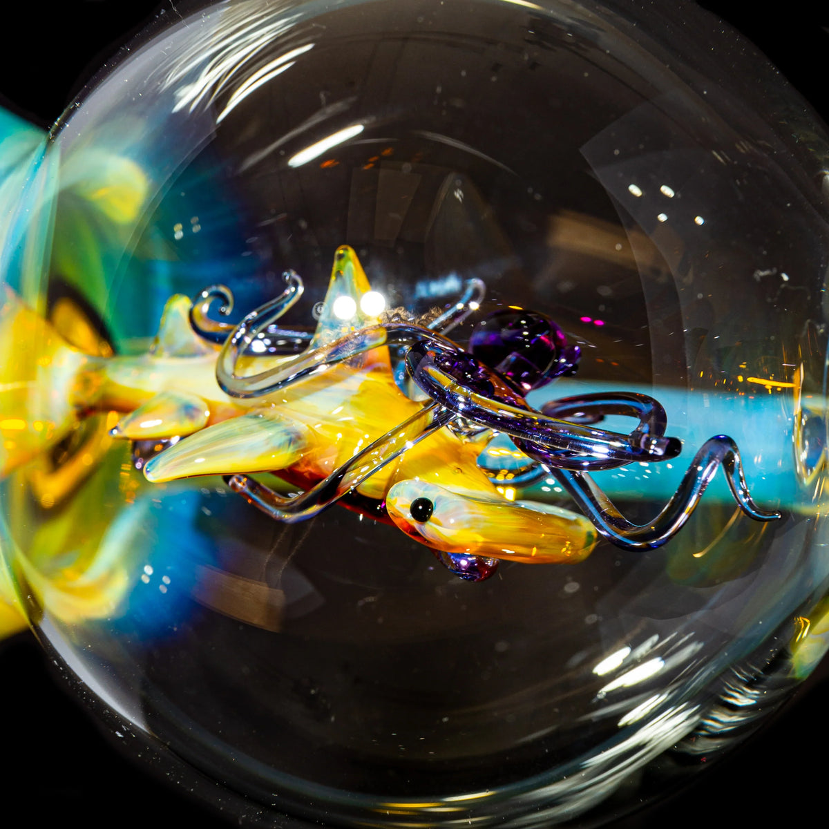 Close-up of a colorful glass art sculpture shaped like a fish with tentacles, inside a clear glass sphere, with vibrant reflections.