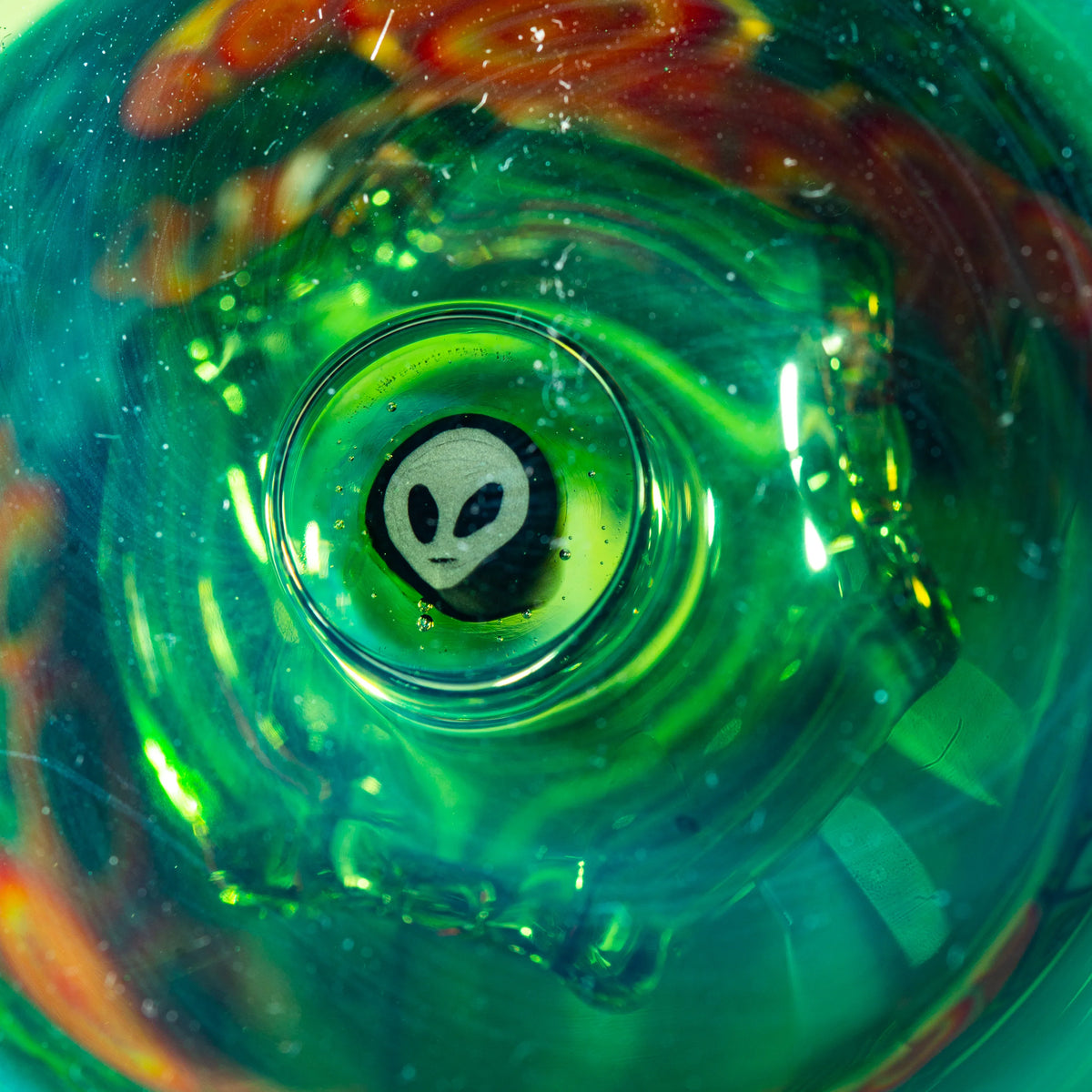 Close-up of green heady glass art with alien face design in center