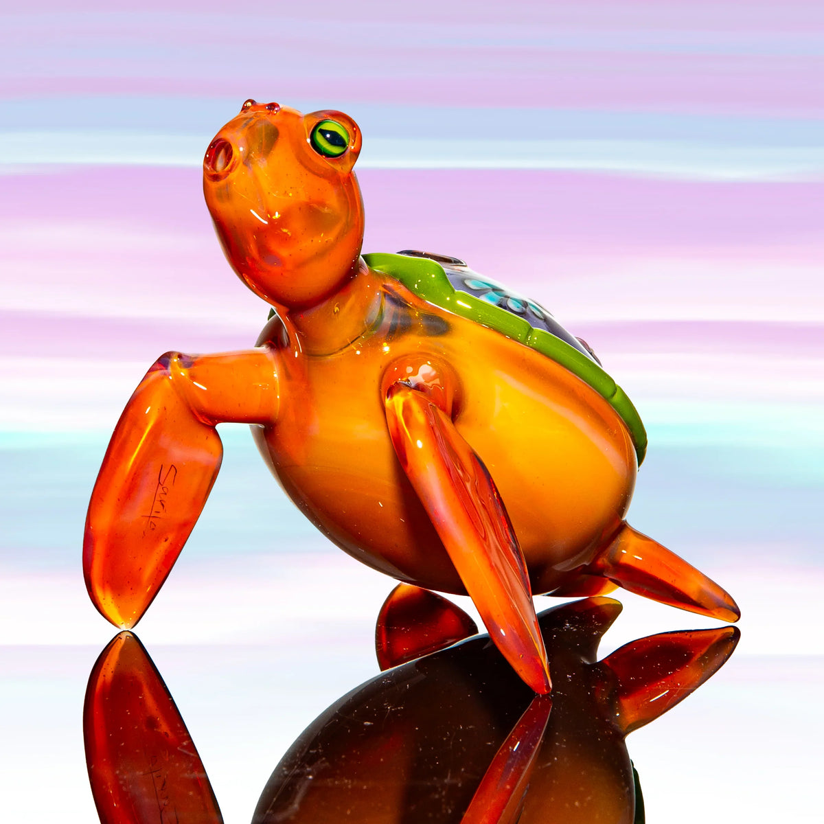 Hand-blown glass turtle art piece with orange and green coloring on a reflective surface