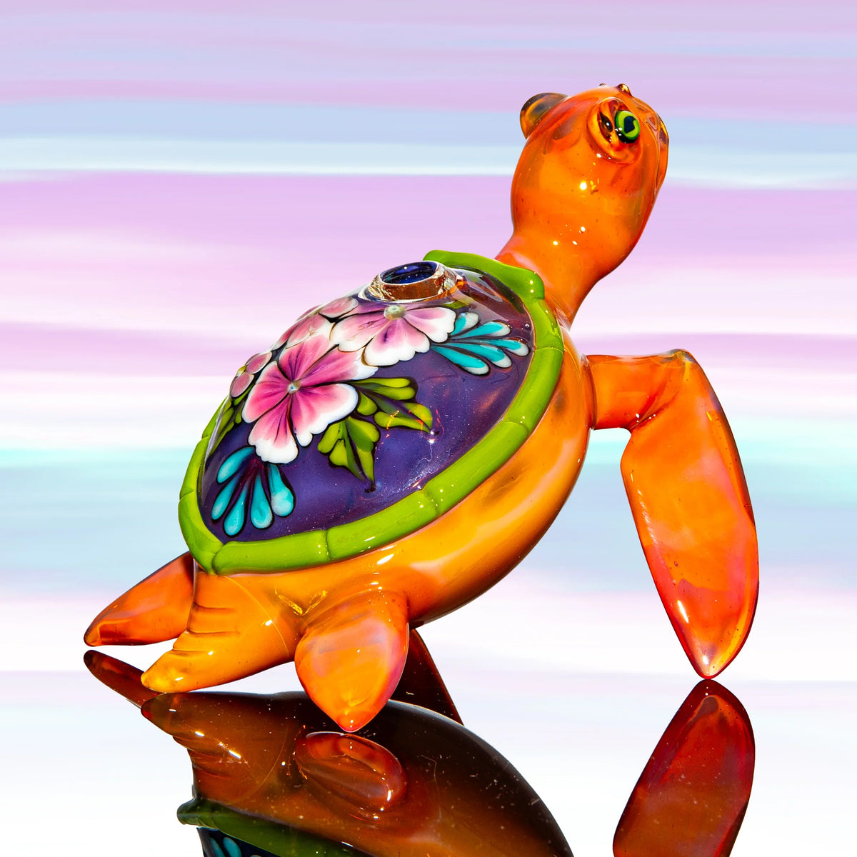Handcrafted glass turtle pipe with floral shell design on a colorful gradient background