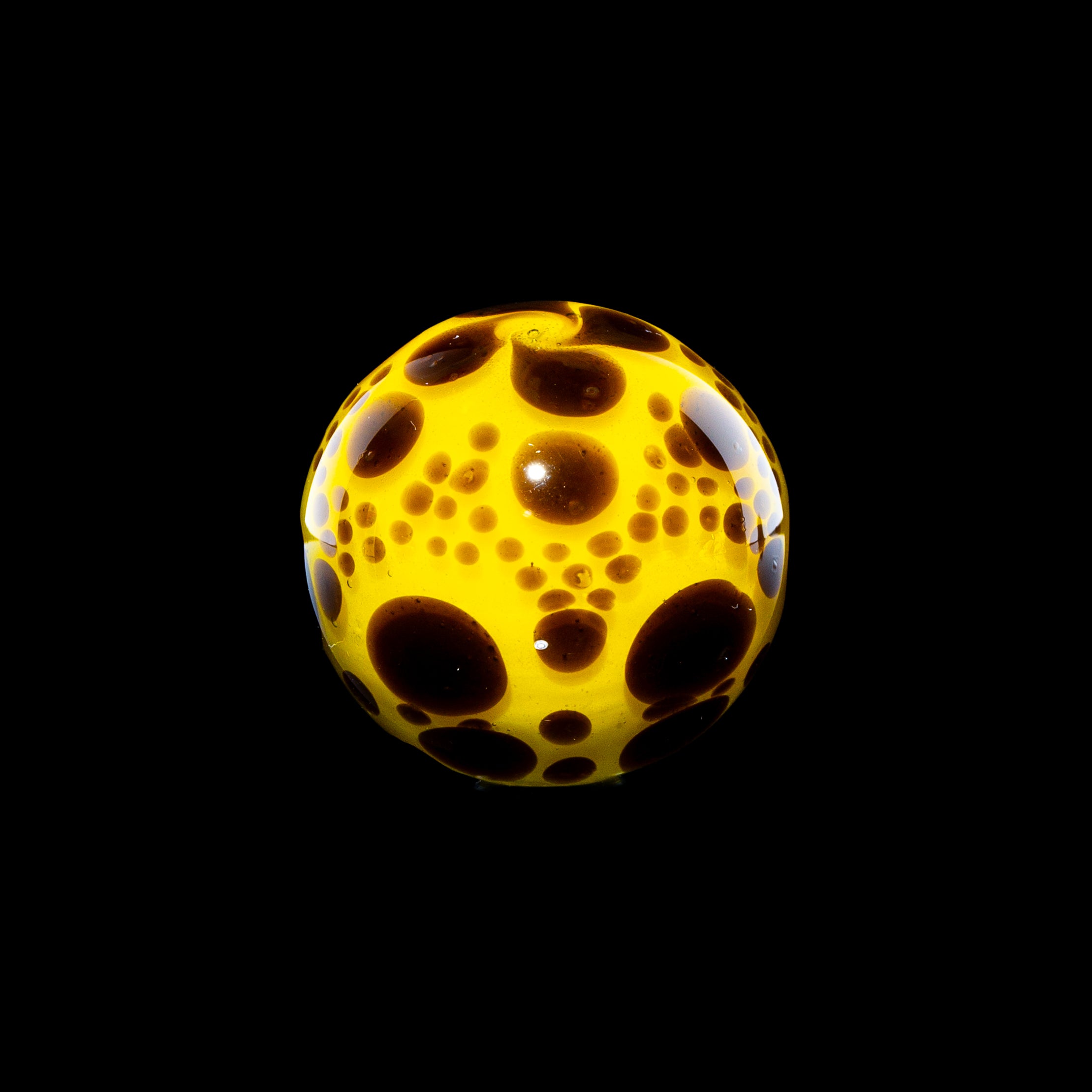 Yellow glass marble with brown bubble patterns on a black background