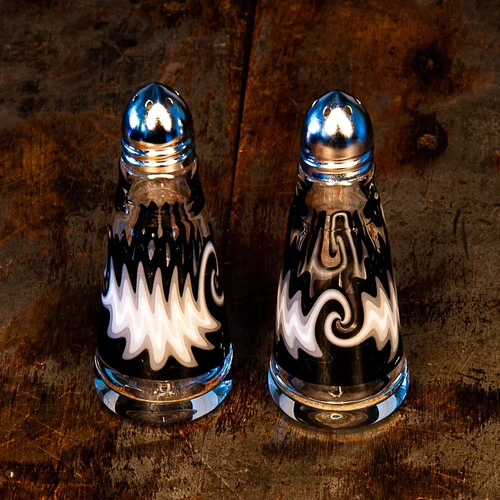 Artistic black and white glass salt and pepper shakers with wavy swirl patterns on wood