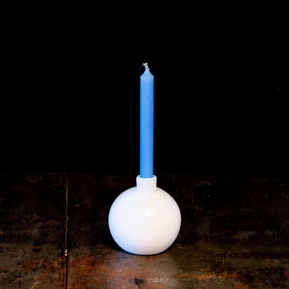 Blue taper candle in a round white glass holder on a rustic wooden surface