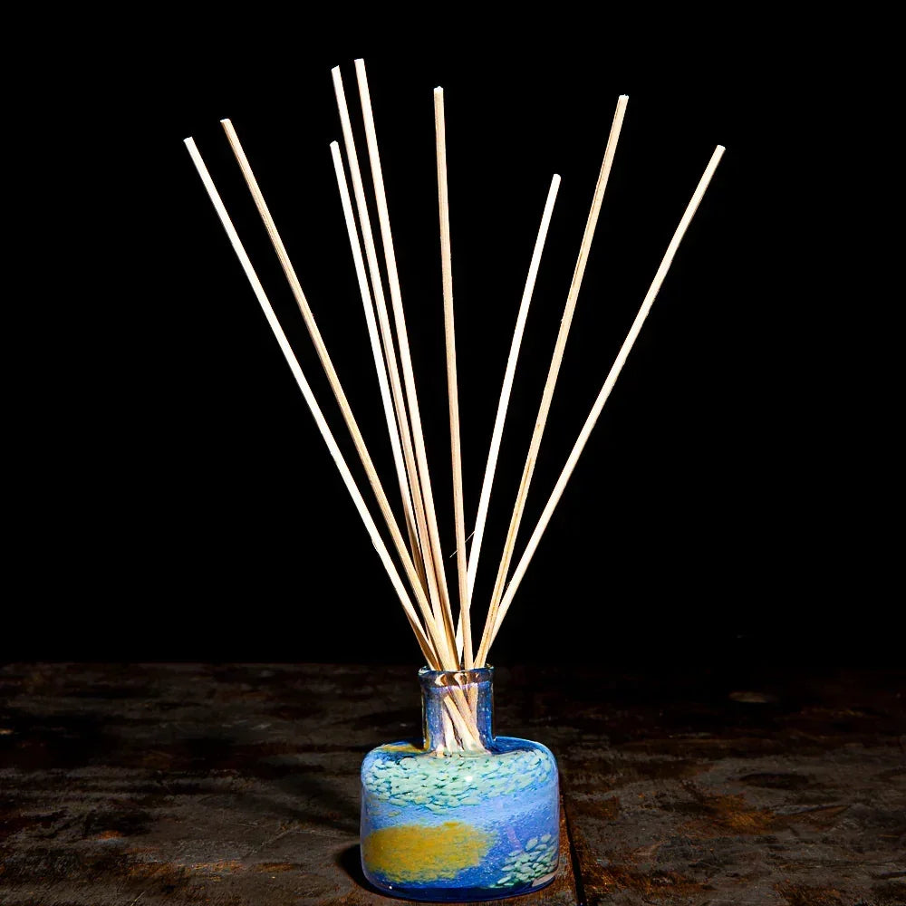 Glass aromatherapy diffuser with wooden reeds in a colorful blue bottle on a dark background