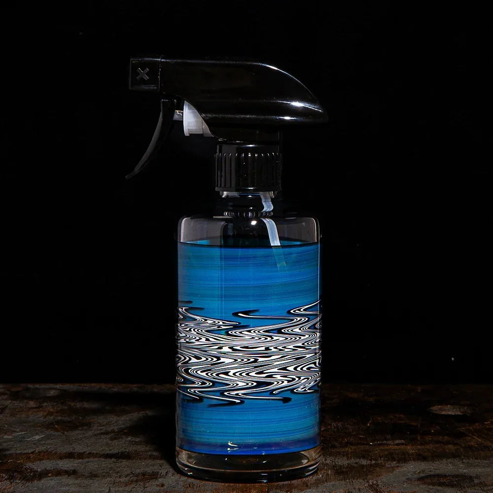 Glass spray bottle with blue and white wavy pattern on a dark background