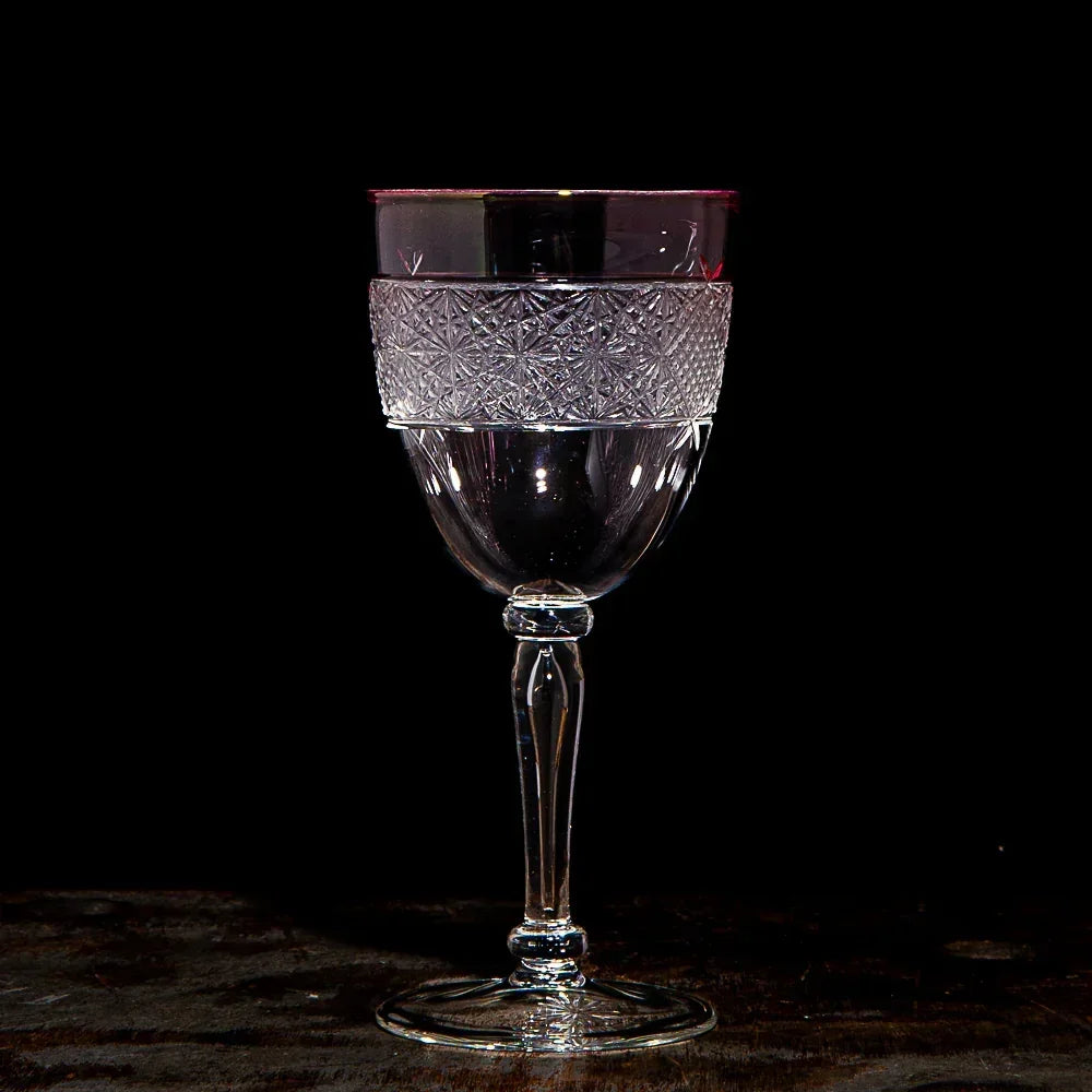 Elegant clear wine glass with etched pattern and red rim on dark background