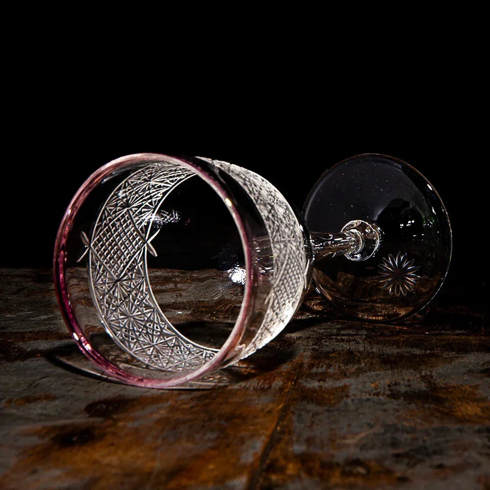 Etched glass goblet with intricate patterns lying on rustic wooden surface