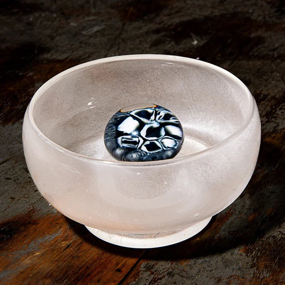 Frosted glass bowl with a decorative black and white marble, displayed on wood surface