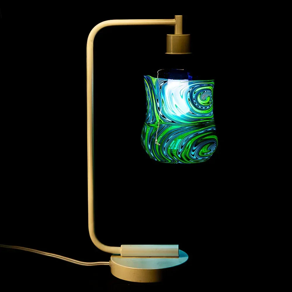 Colorful glass art piece with green and blue swirls illuminated on a modern lamp stand