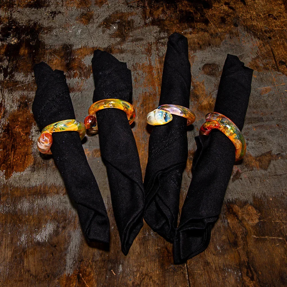 Colorful glass napkin rings on black cloth napkins atop rustic wooden table