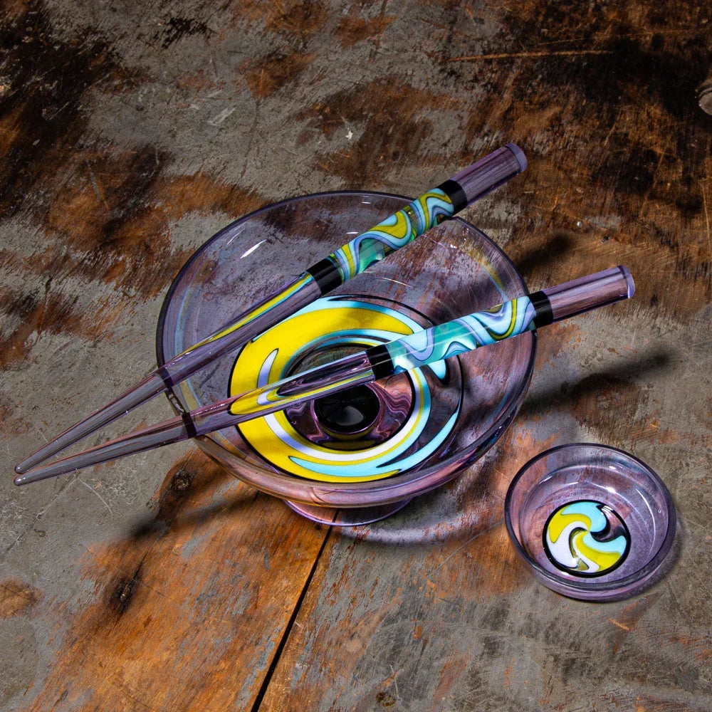Colorful glass chopsticks with matching swirled glass bowls on rustic wood surface